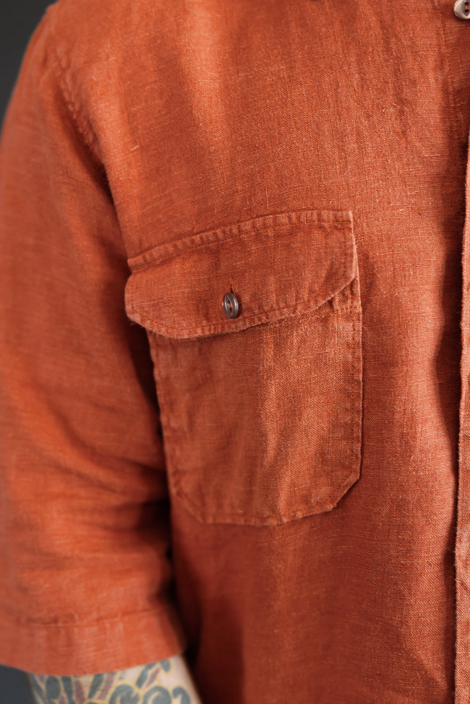 Close-up of rust linen shirt chest pocket, button detail, male model 5'9