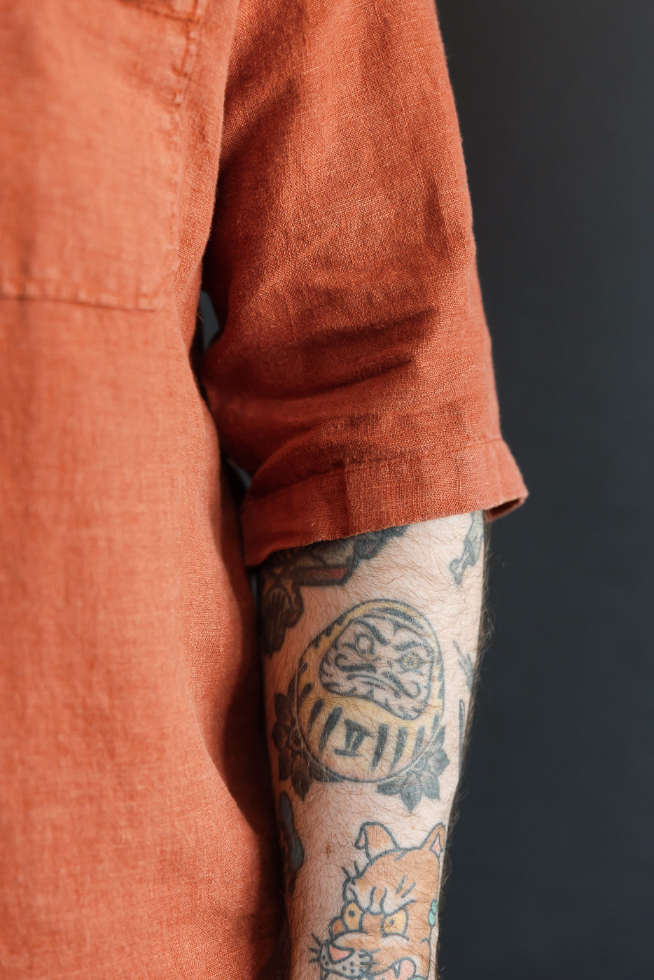 Close-up of male model's arm in rust orange shirt, showcasing sleeve hem and fabric texture