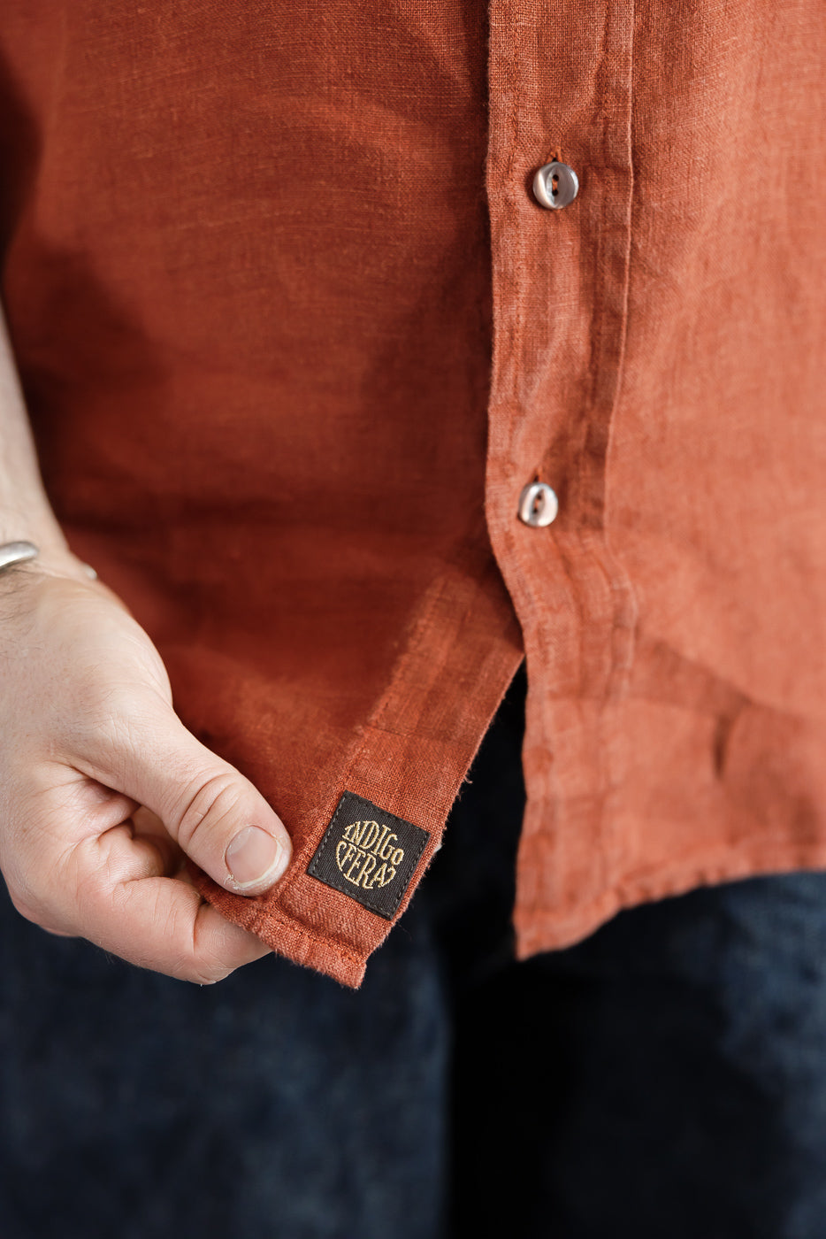 Close-up of rust linen shirt hem with ADIGE VERA tag, worn by male model, 5'9