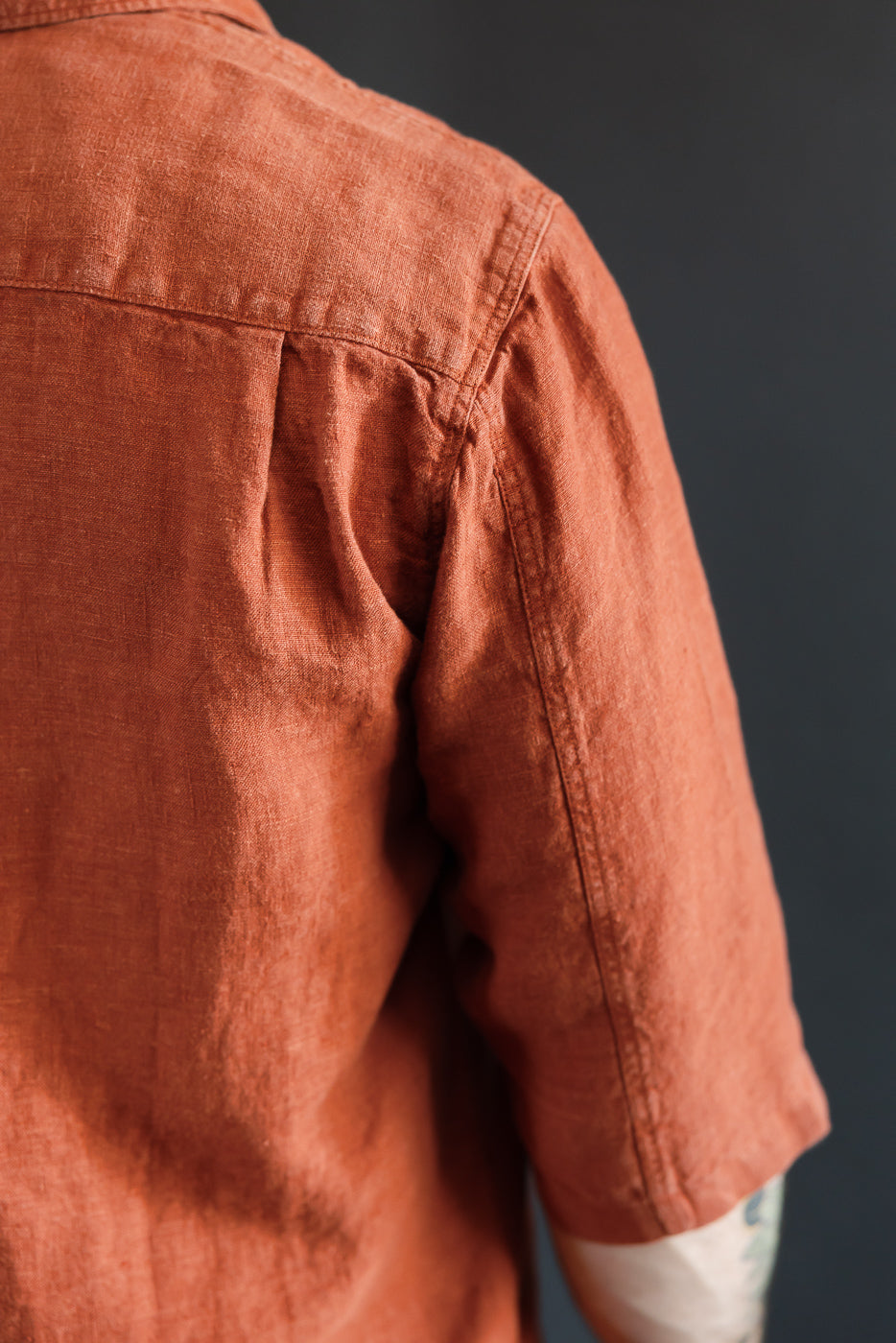 Close-up of male model's back, showcasing rust linen shirt with shoulder seam detail, 5'9
