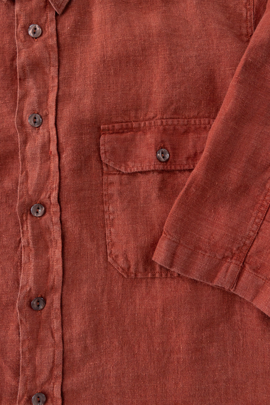 Close-up front view of rust linen shirt, button details, chest pocket, and sleeve texture