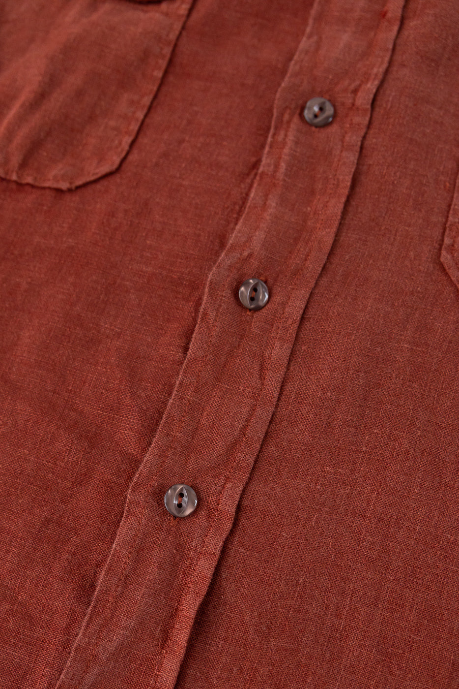 Close-up front view of rust linen shirt showing button placket, chest pocket, and textured fabric weave