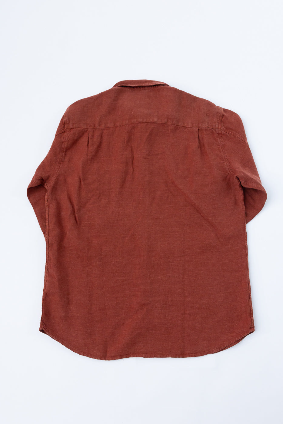 Rust-colored linen shirt back view, flat lay, showing curved hem and shoulder seams