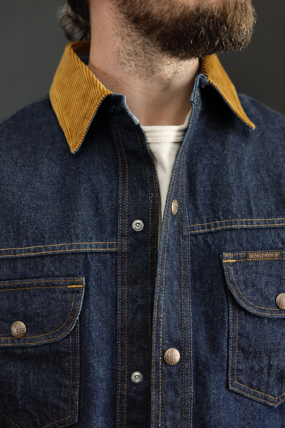 Close-up front view of male model wearing indigo denim shirt with corduroy collar, button details, and chest pockets.