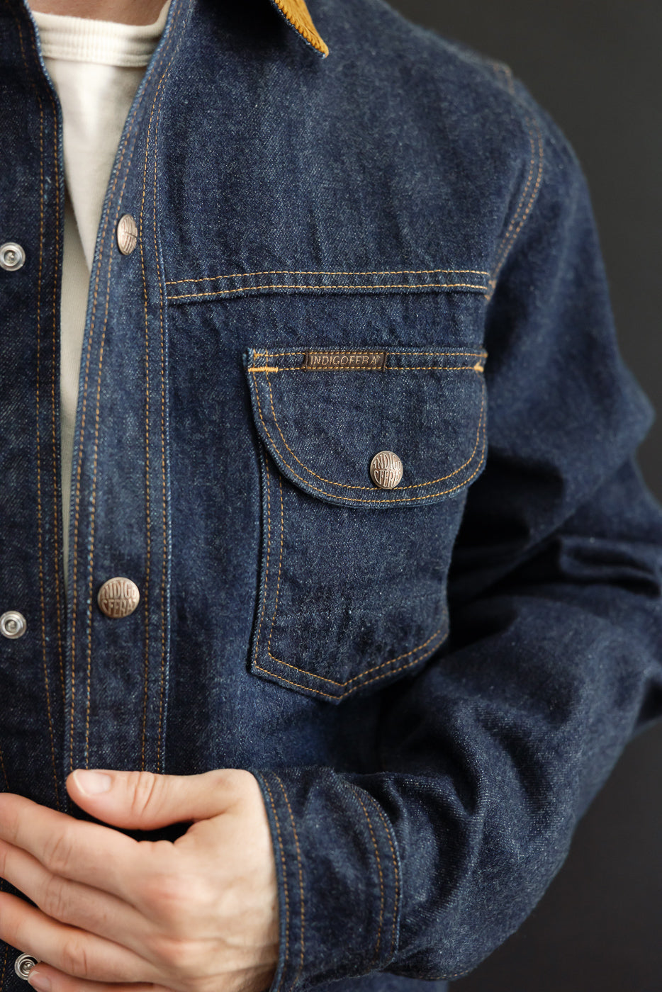 Close-up of male model's front, showcasing denim jacket with chest pocket, button details, and selvedge fabric.