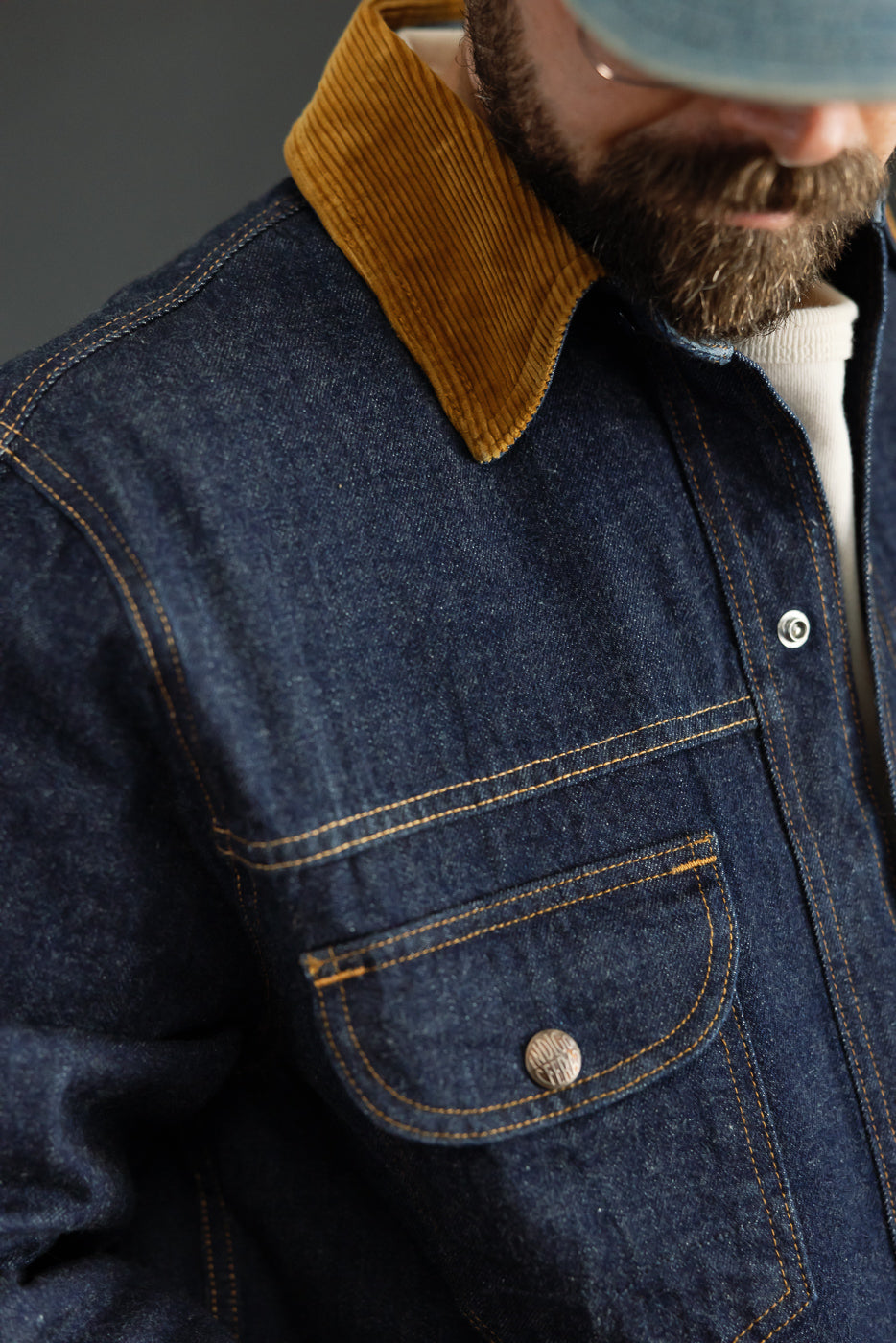 Close-up front view of male model in denim jacket with corduroy collar, chest pocket, and contrast stitching