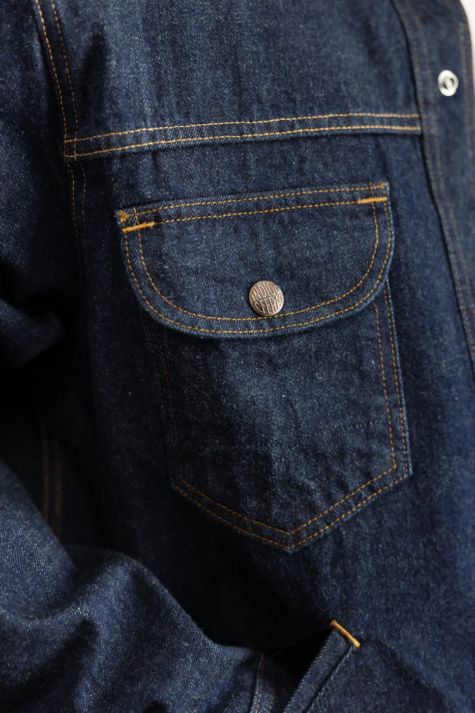 Close-up of front left chest pocket on indigo denim shirt with button detail and orange stitching