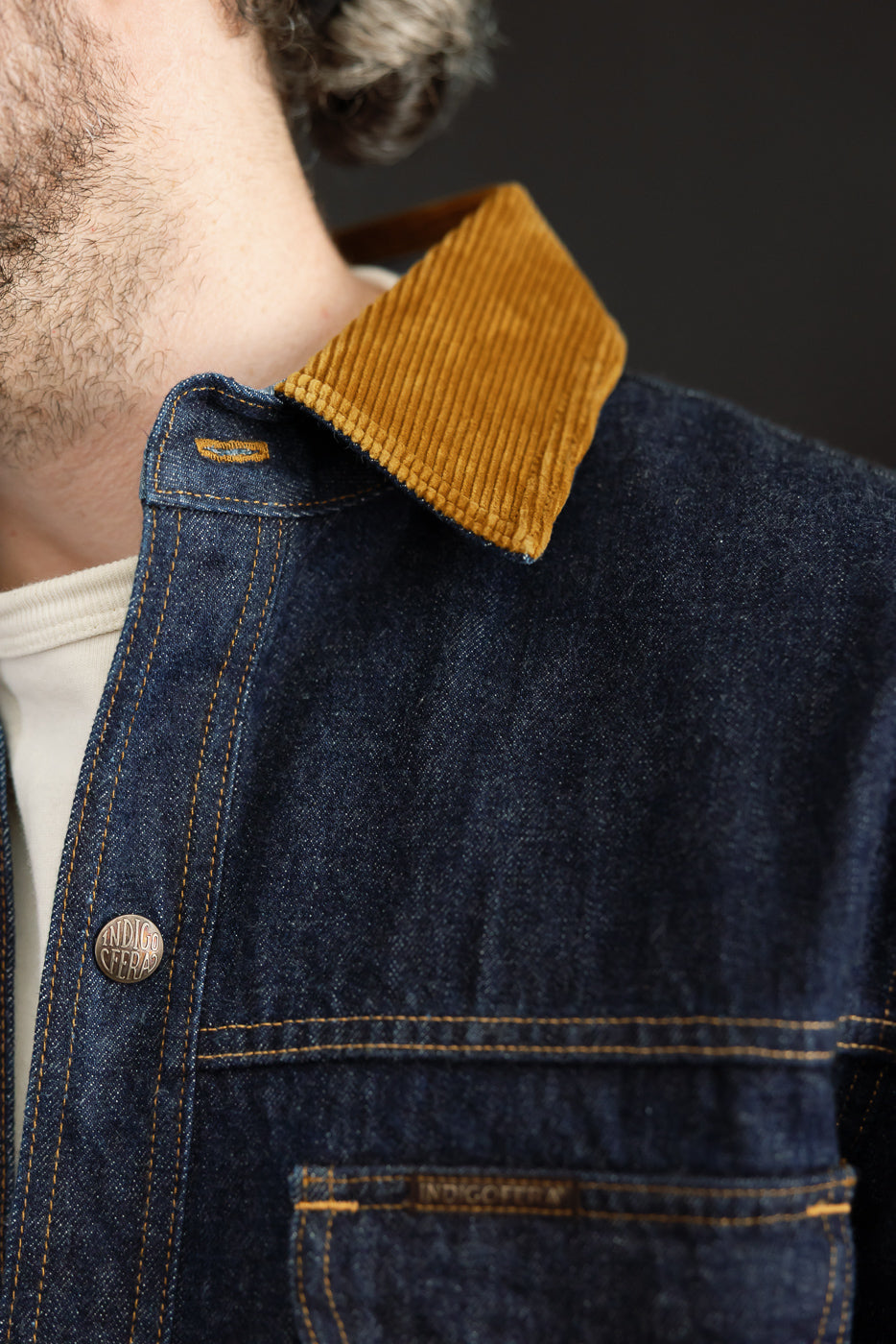 Close-up of male model's denim shirt front, showcasing corduroy collar, button, and pocket details.