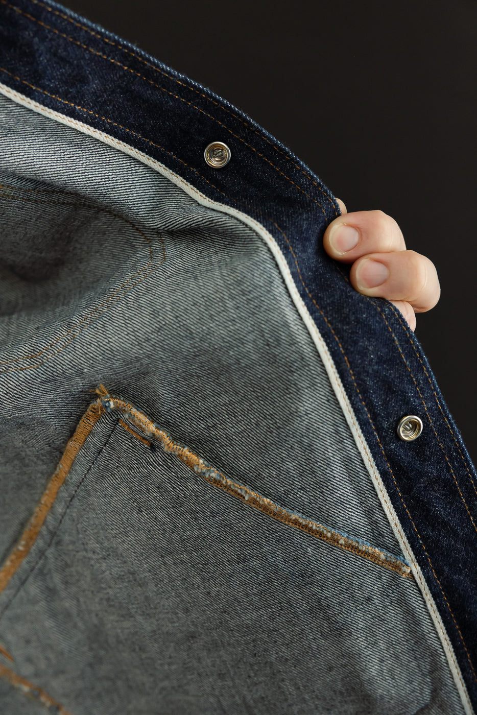 Close-up of selvedge denim jacket front, showing button details, stitching, and fabric texture