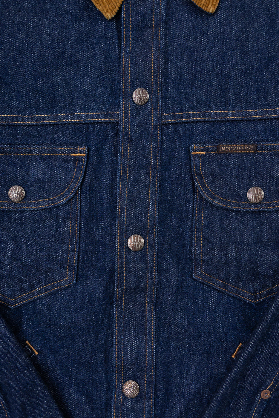 Close-up front view of indigo denim shirt with corduroy collar, branded buttons, and chest pockets.