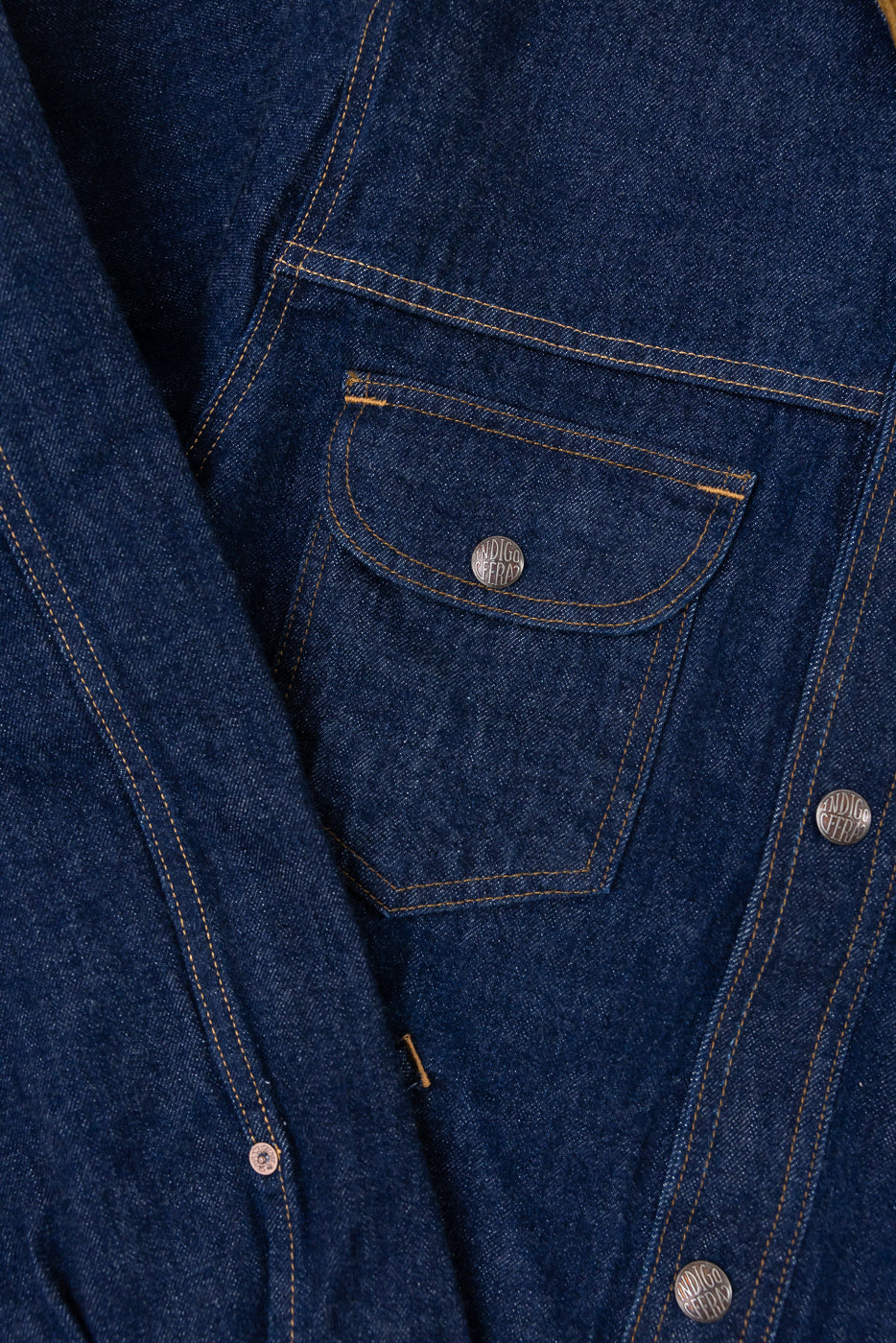 Close-up of indigo denim jacket front, showcasing chest pocket, button, and stitching details