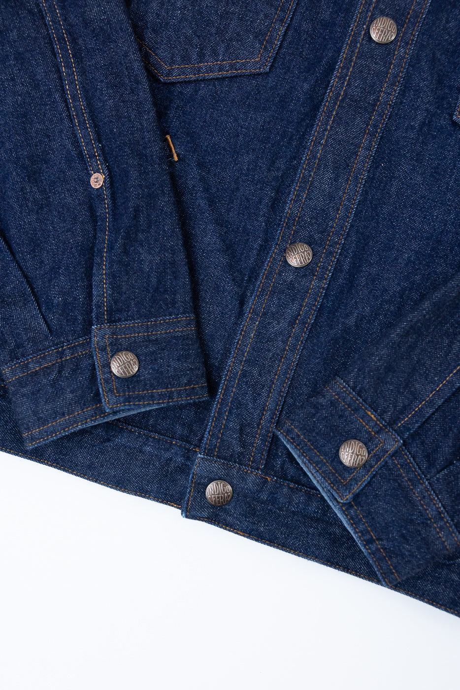 Close-up front view of indigo denim jacket with branded buttons and orange stitching details