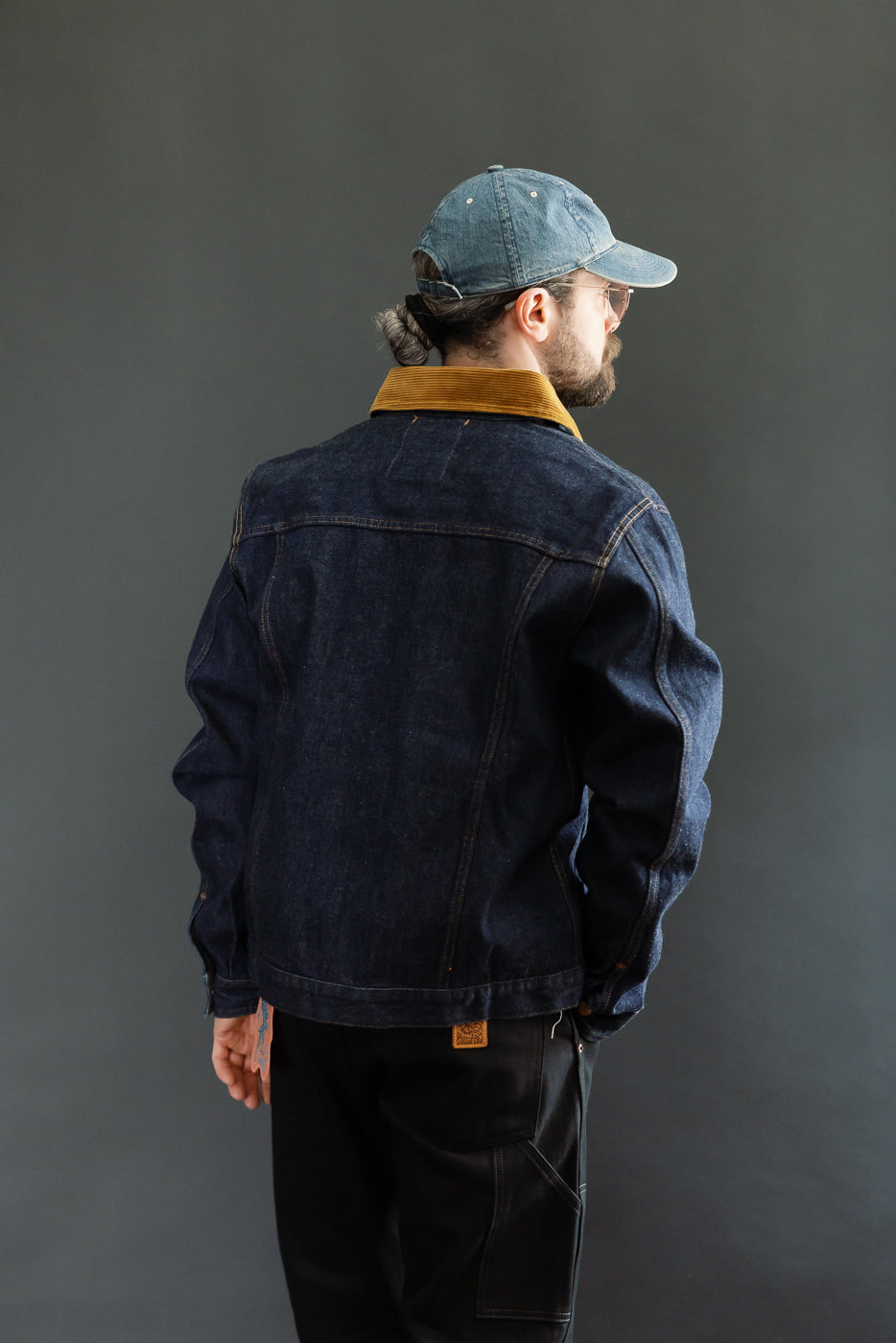 Back view of male model in dark denim jacket with corduroy collar, full body shot