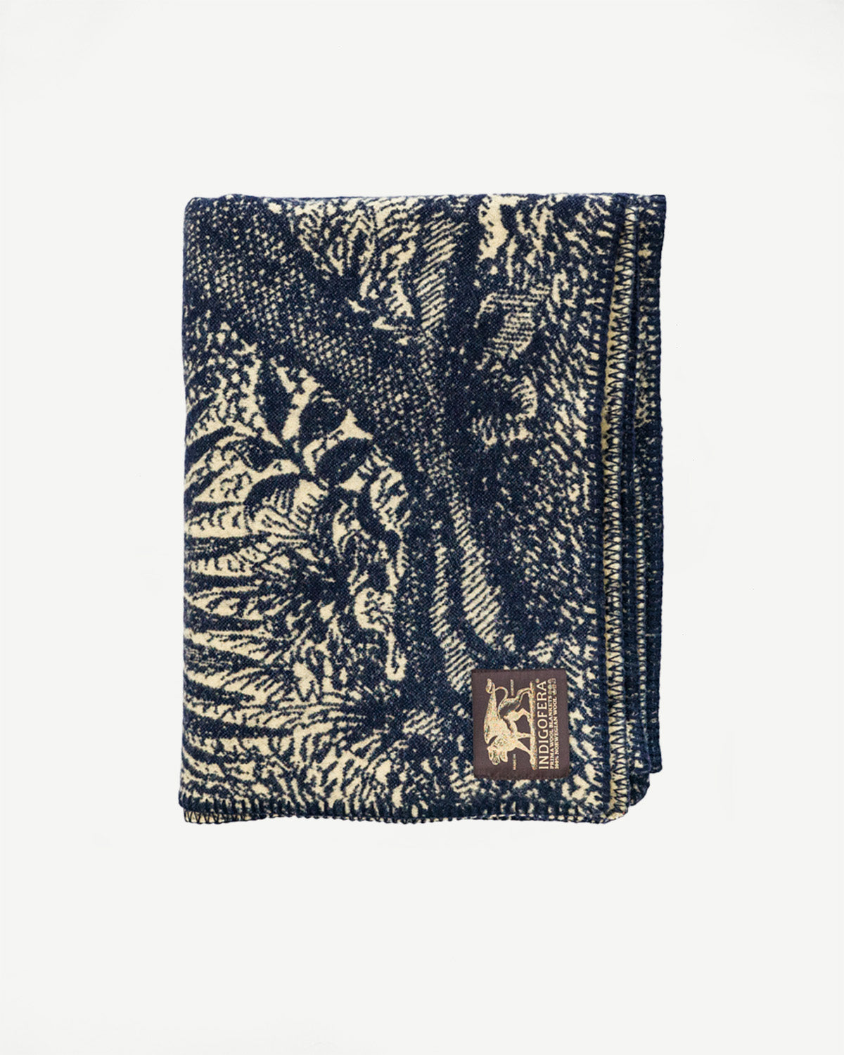 Flat lay, front view of folded beige and navy patterned blanket with visible woven tag detail.