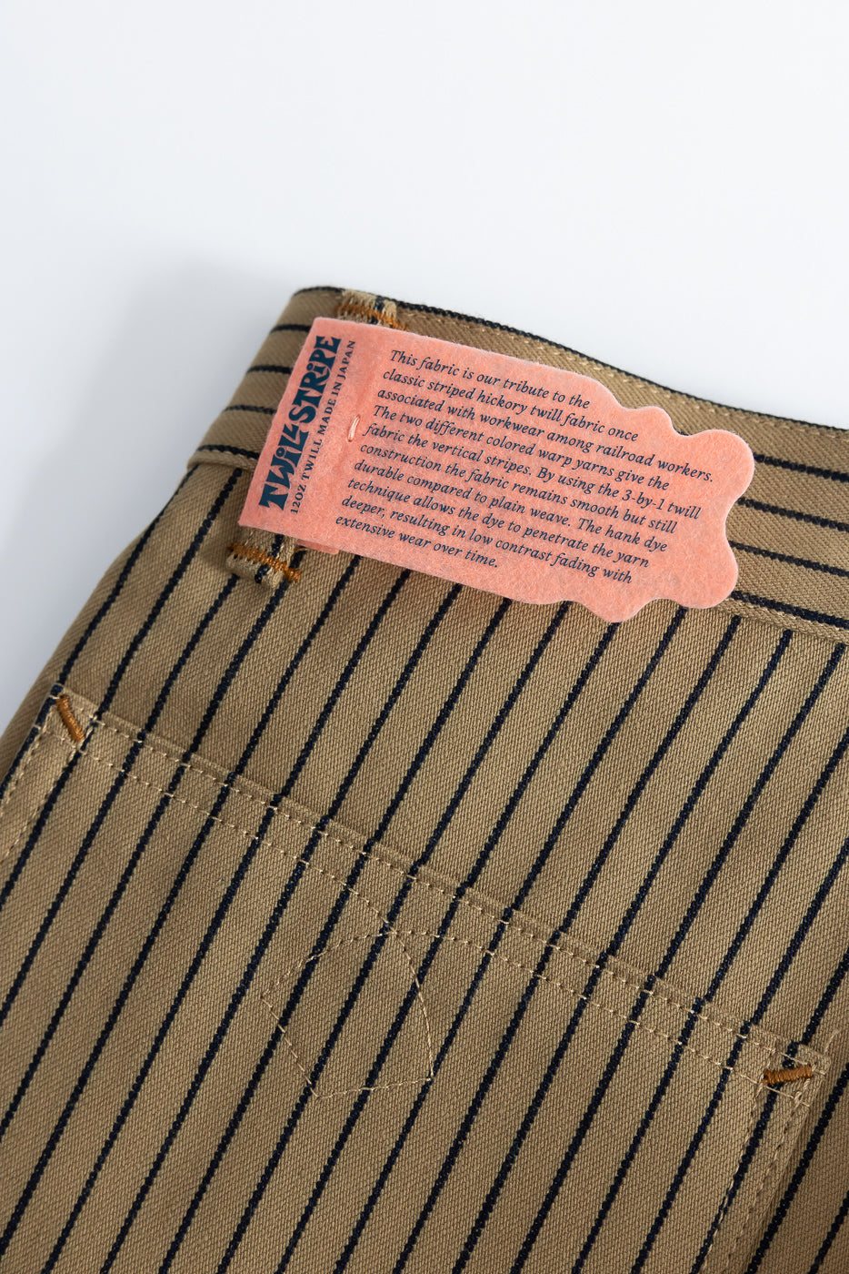 Close-up of back of beige and indigo striped pants showing pocket stitching and fabric tag detail.