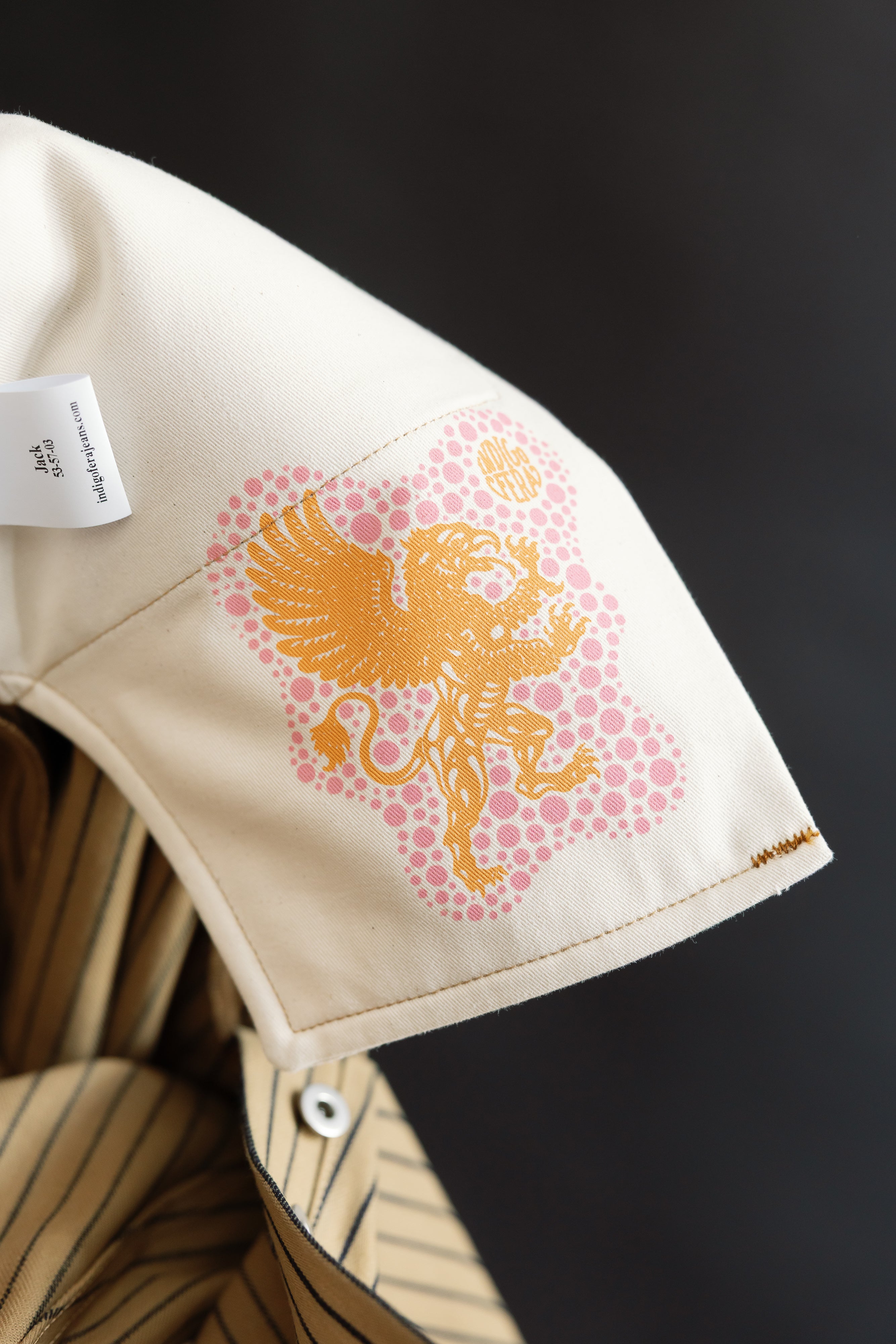 Close-up of the inside collar of a beige and indigo striped shirt showing a gold lion graphic and fabric tag.