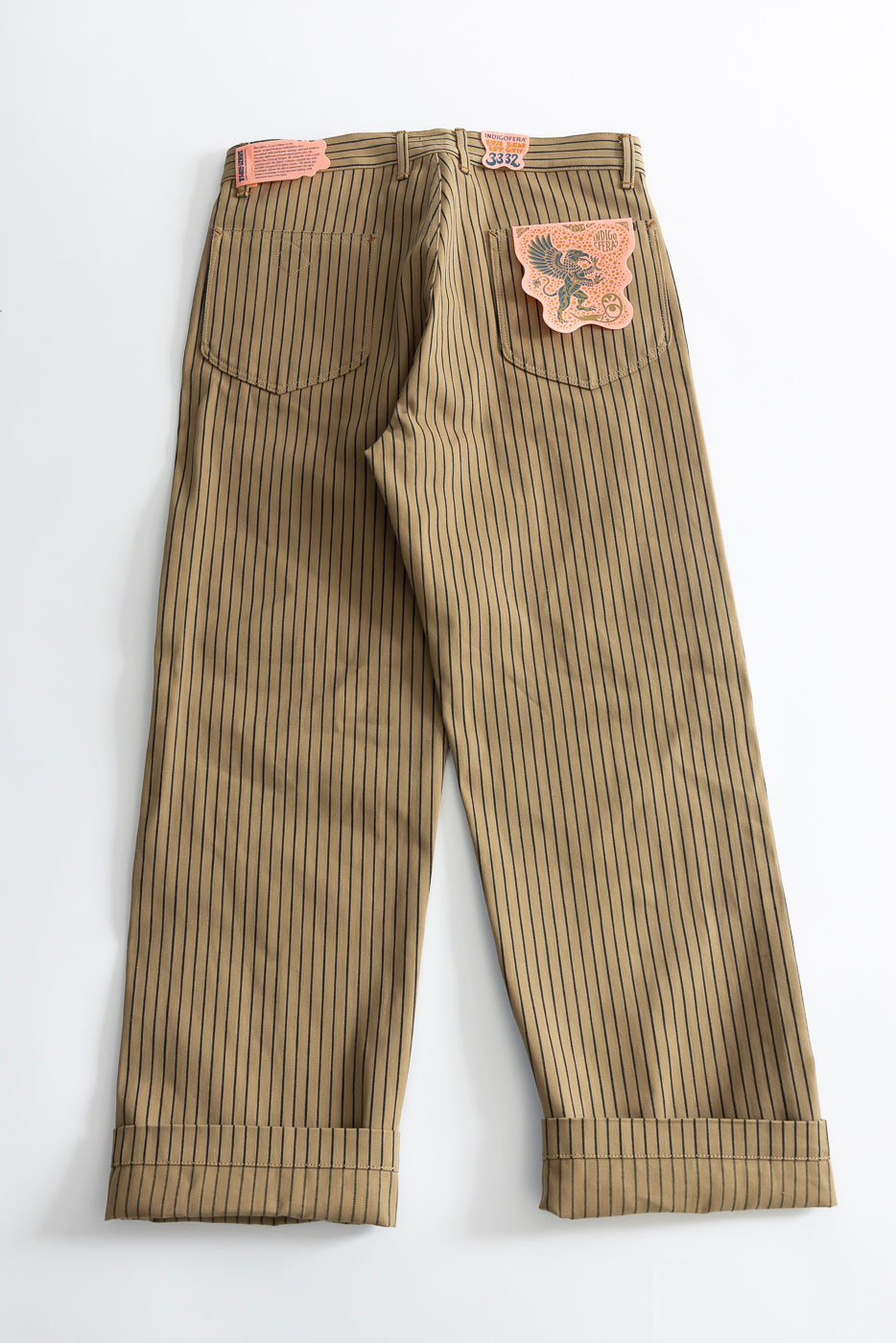 Flat lay of beige and indigo pinstripe pants, back view, showing rear pockets and leather patch detail.