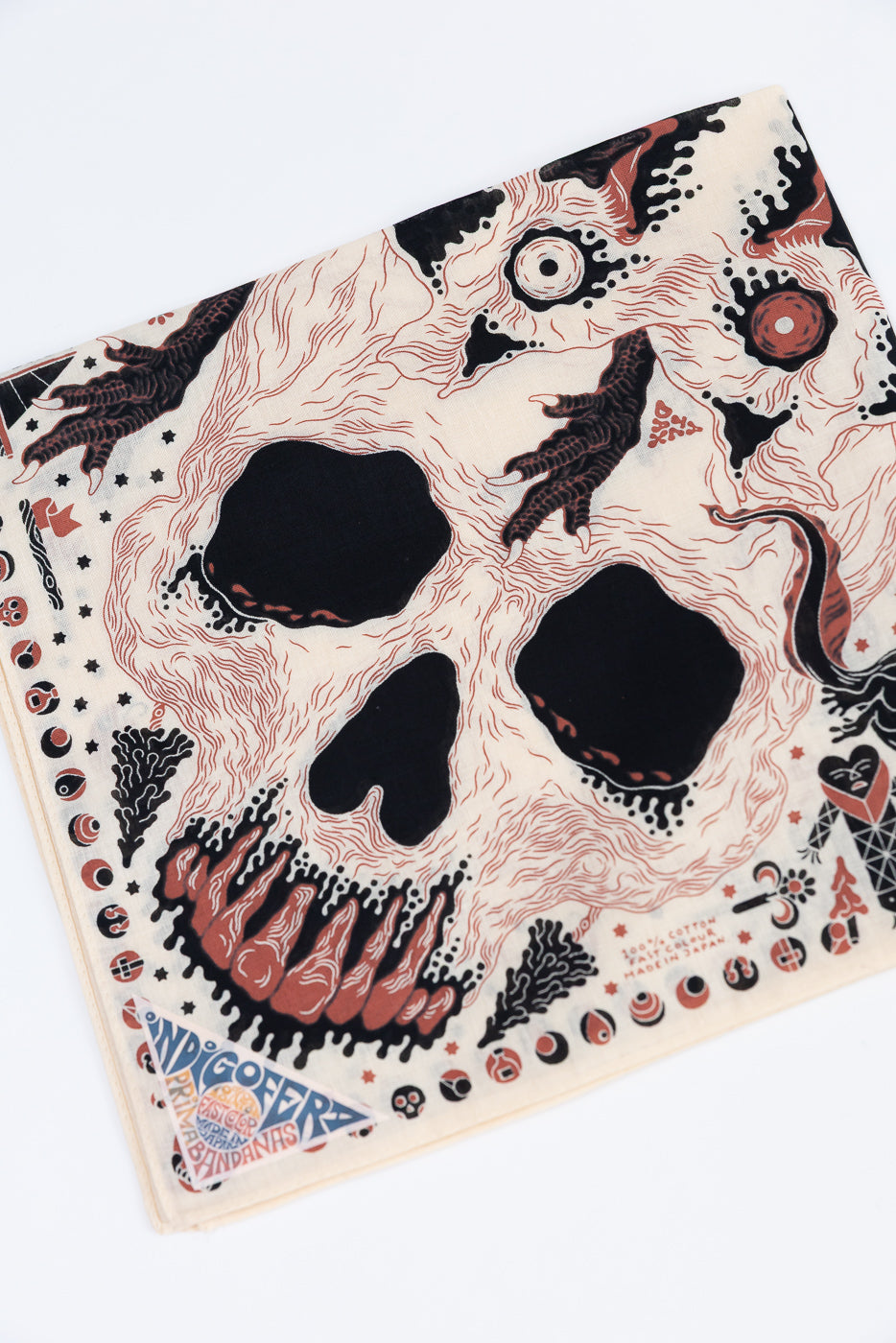 Close-up flat lay of the front of an Indigofera bandana with a skull and bone graphic print.