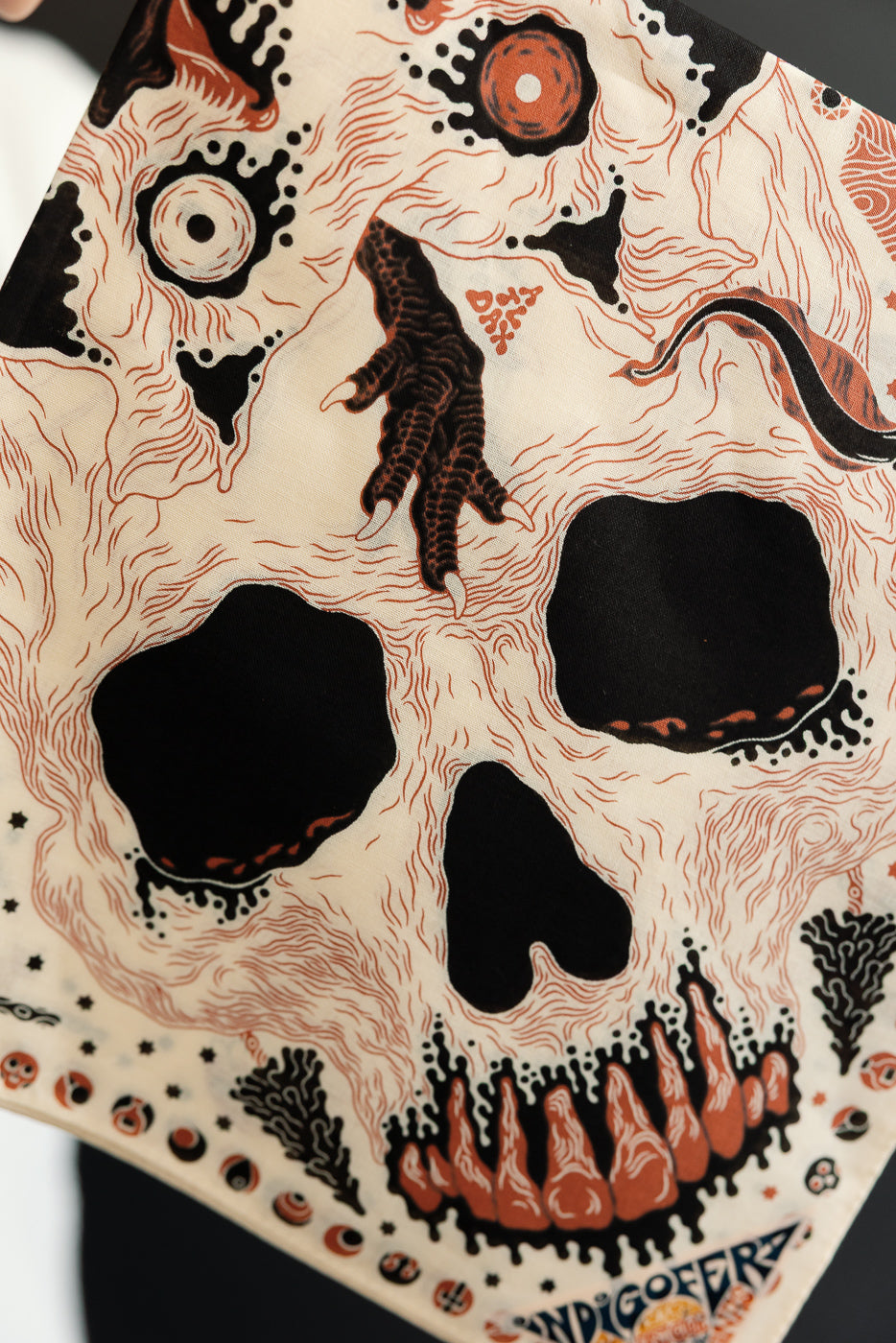 Close-up of front side of a scarf featuring a surreal skull graphic with intricate line work.