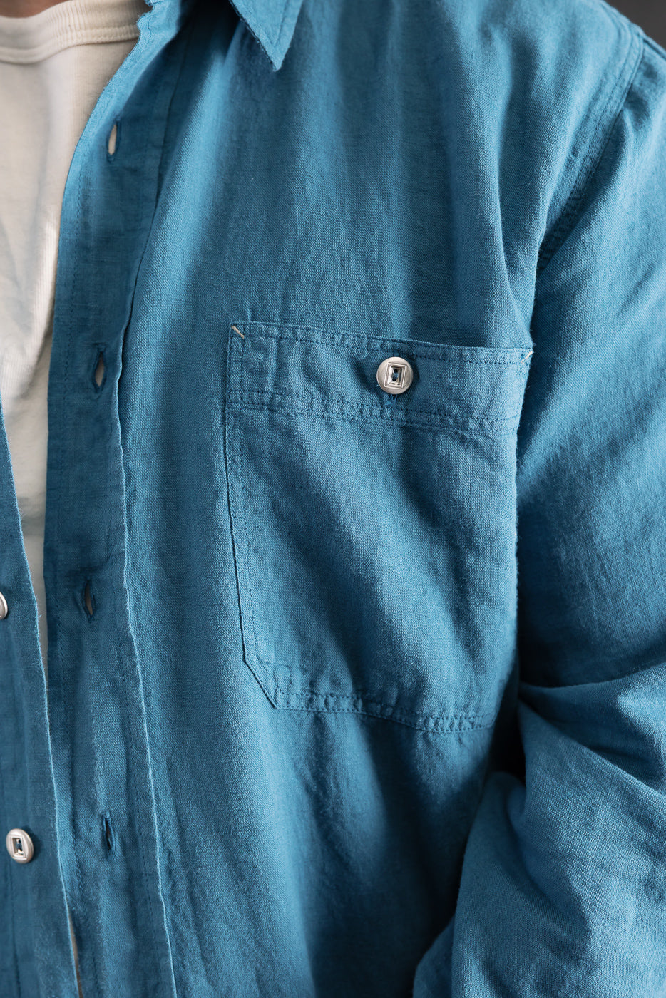 Close-up of front chest pocket and button on ocean blue canvas shirt, male model 5'9