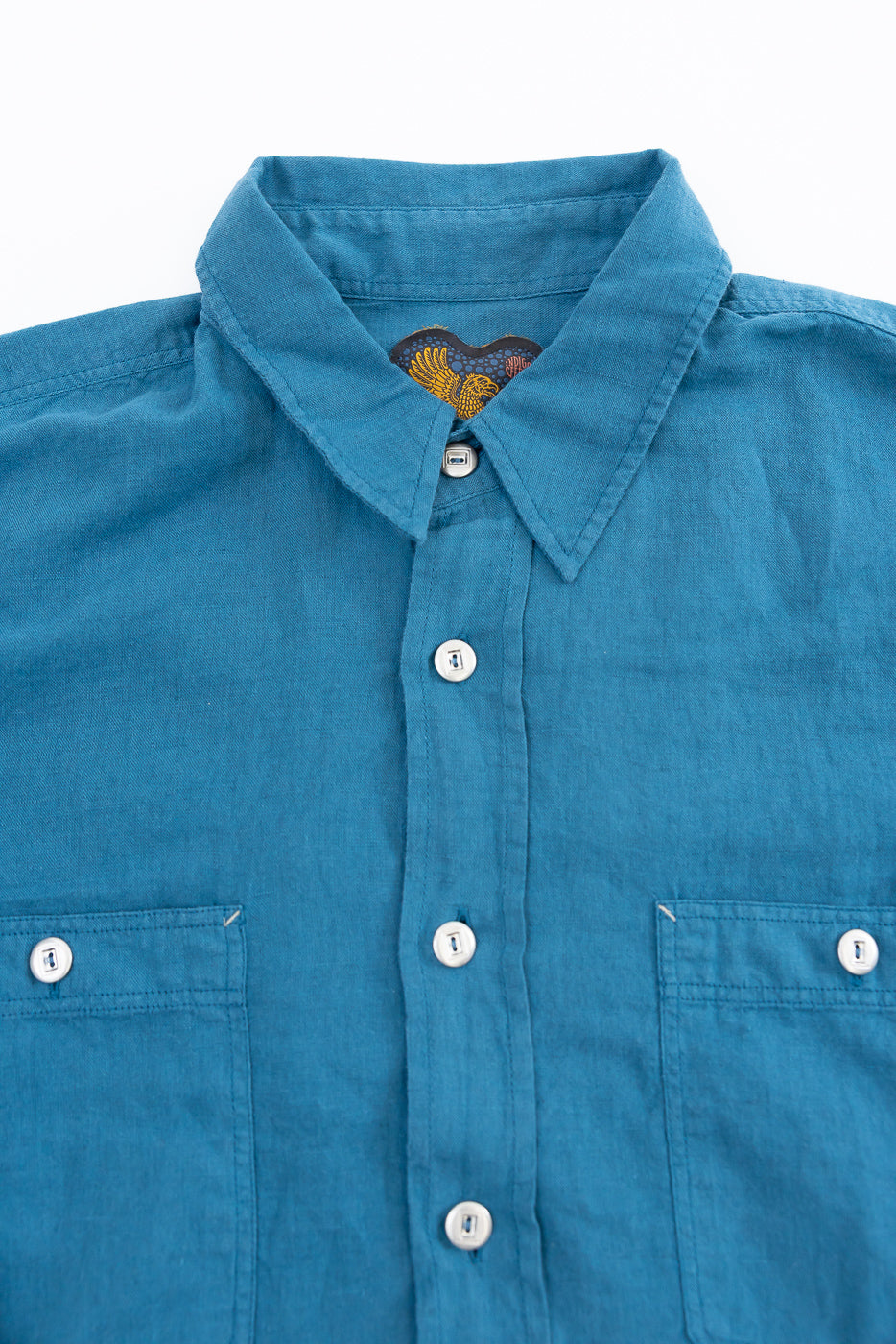Close-up front view of Indigofera McAllen blue canvas shirt showing white buttons, pockets, and collar detail.