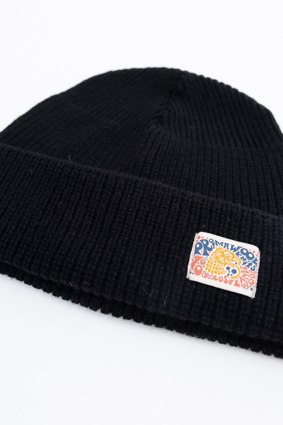 Close-up of the front cuff of a black ribbed knit beanie featuring a colorful graphic tag.