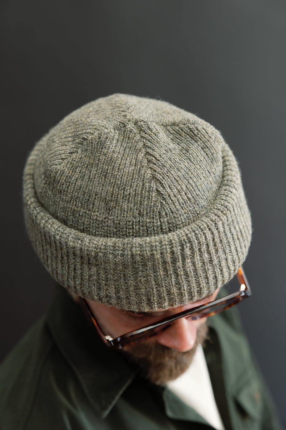 Close-up front view of a male model wearing a textured olive green ribbed knit beanie.