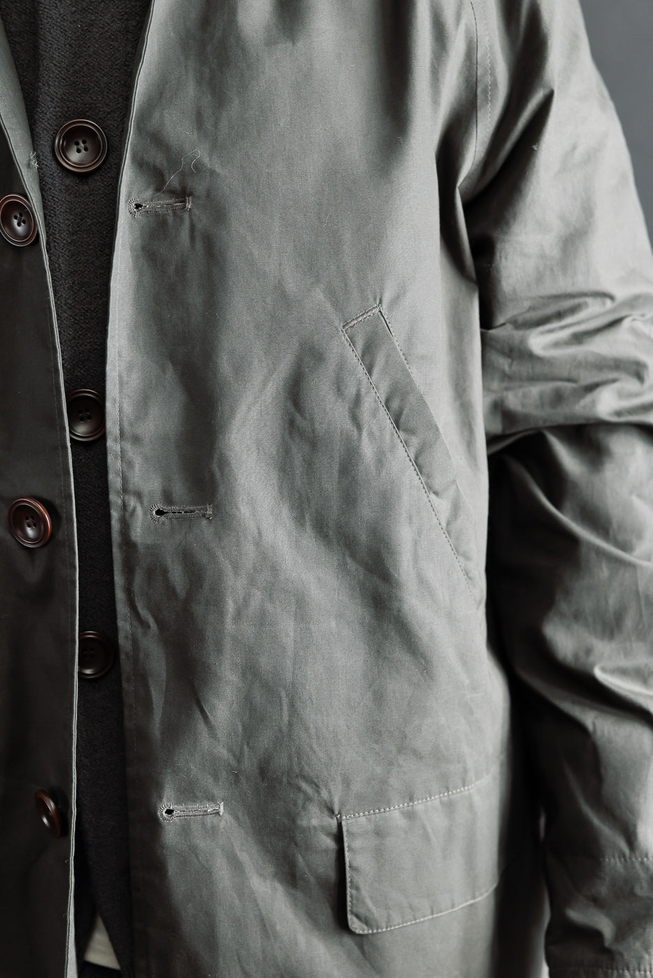 Close-up front view of Indigofera Raven coat in dark grey coated cotton twill, single-breasted with button details, worn by a male model 5'9