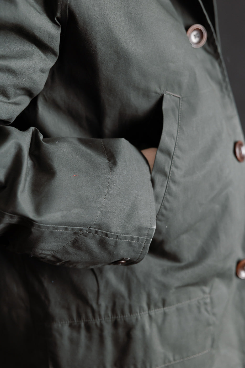 Close-up of men's Indigofera Raven Coat front pocket, coated cotton twill, dark grey, button detail, model is 5'9, 165lbs, athletic build.