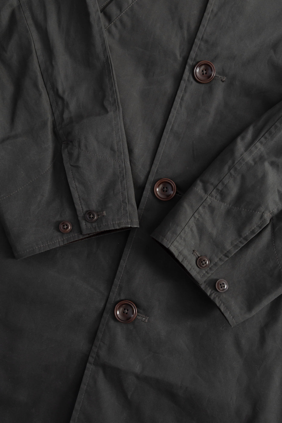 Close-up of Indigofera Raven Coat front, dark grey coated cotton twill, brown buttons, cuff detail