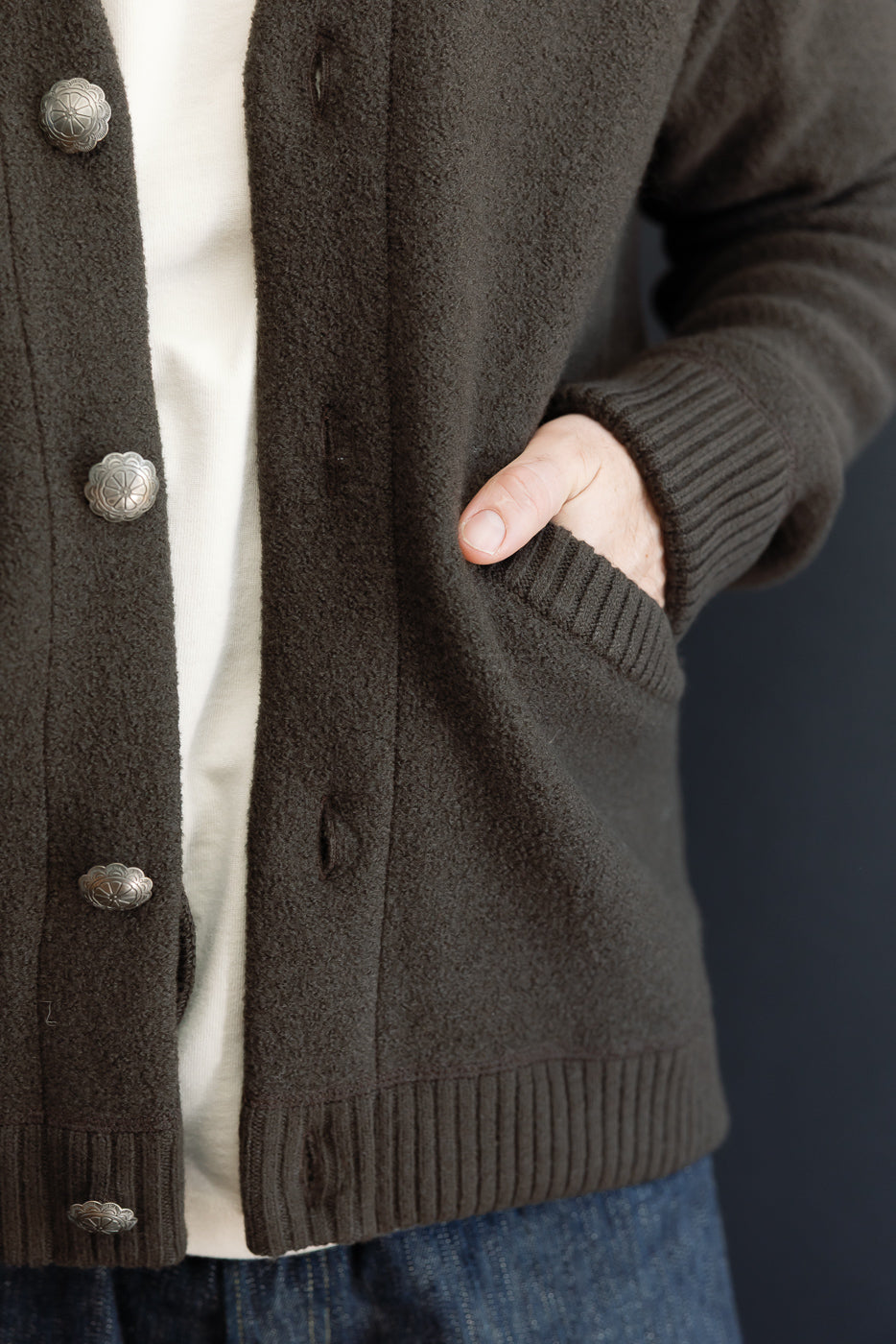 Close-up side view of a dark brown textured cardigan showing the pocket and ribbed cuff on a male model.