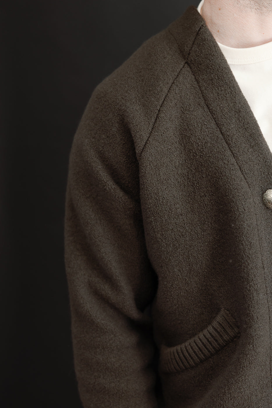 Close-up side view of a male model wearing a brown textured cardigan, showing the sleeve and pocket.