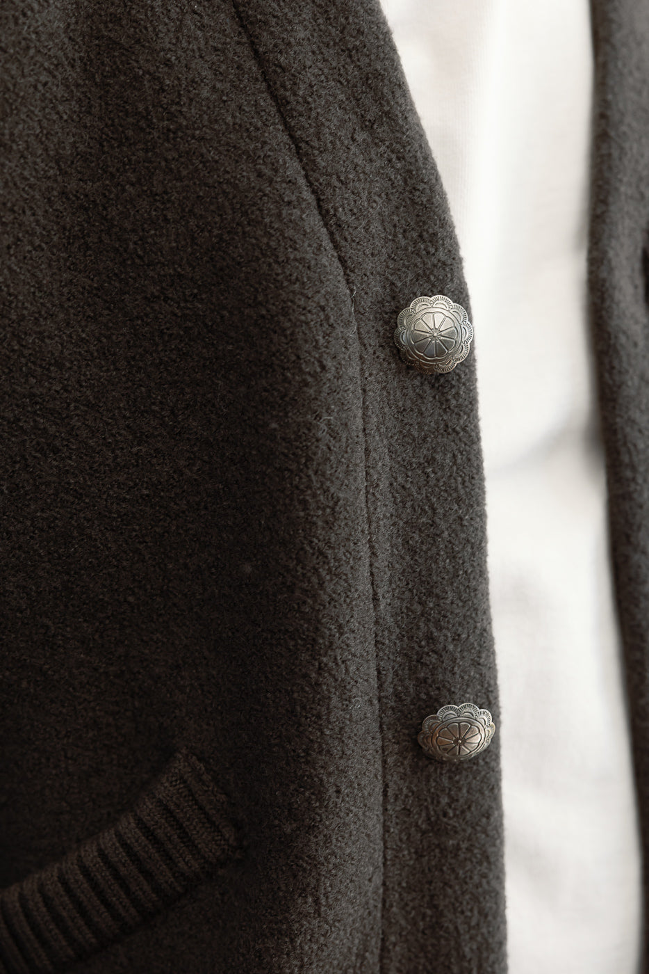 Close-up of the front right side of a dark charcoal textured cardigan showing decorative metal buttons.