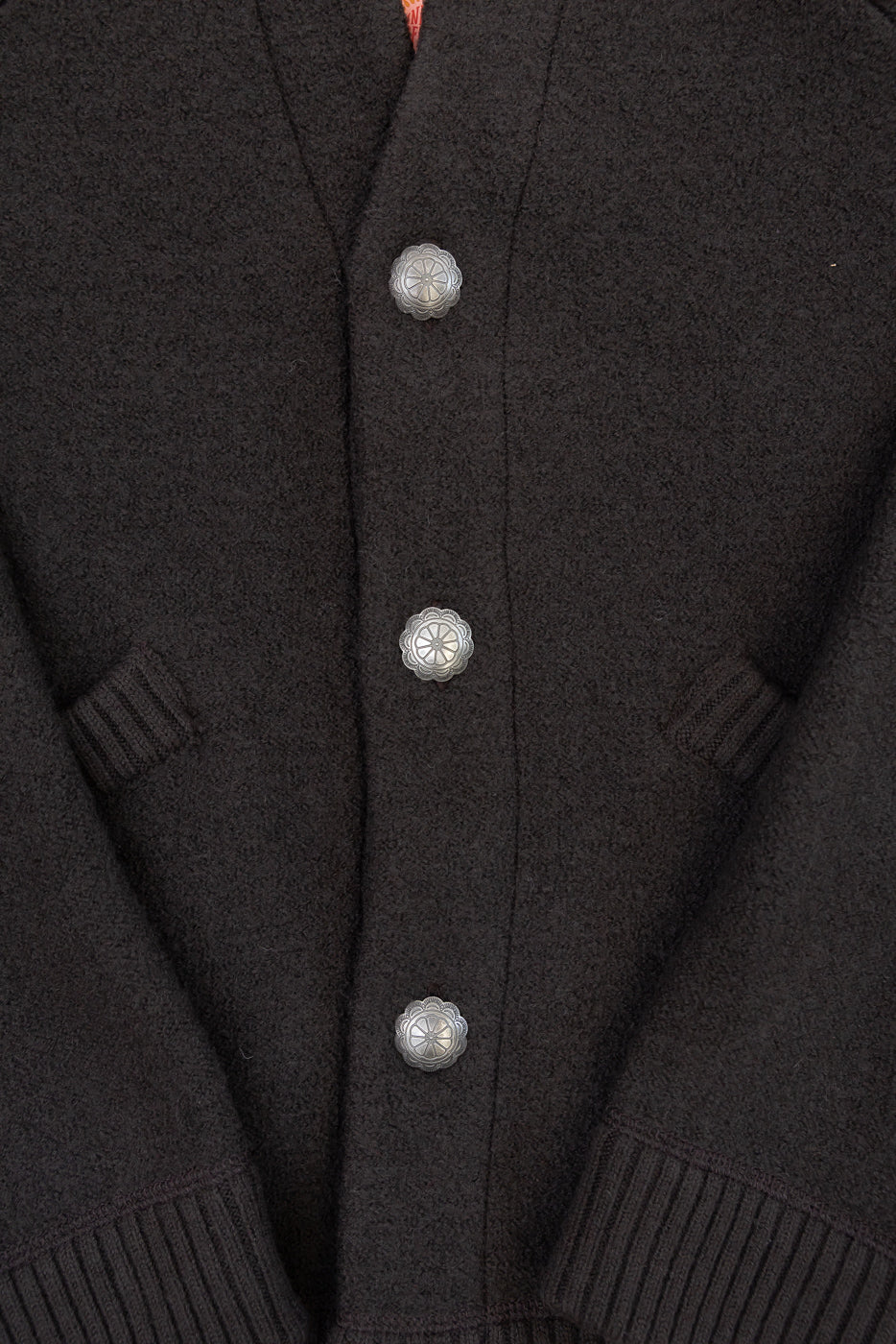 Close-up of the front of a black wool cardigan showing decorative silver buttons and fabric texture.