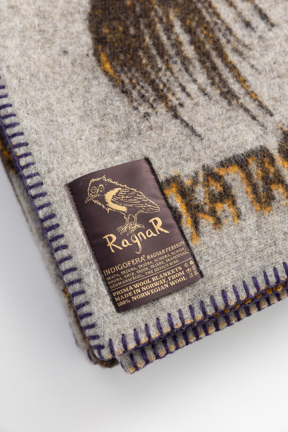 Close-up of Indigofera x Ragnar Persson grey wool blanket corner showing label, trim, texture.
