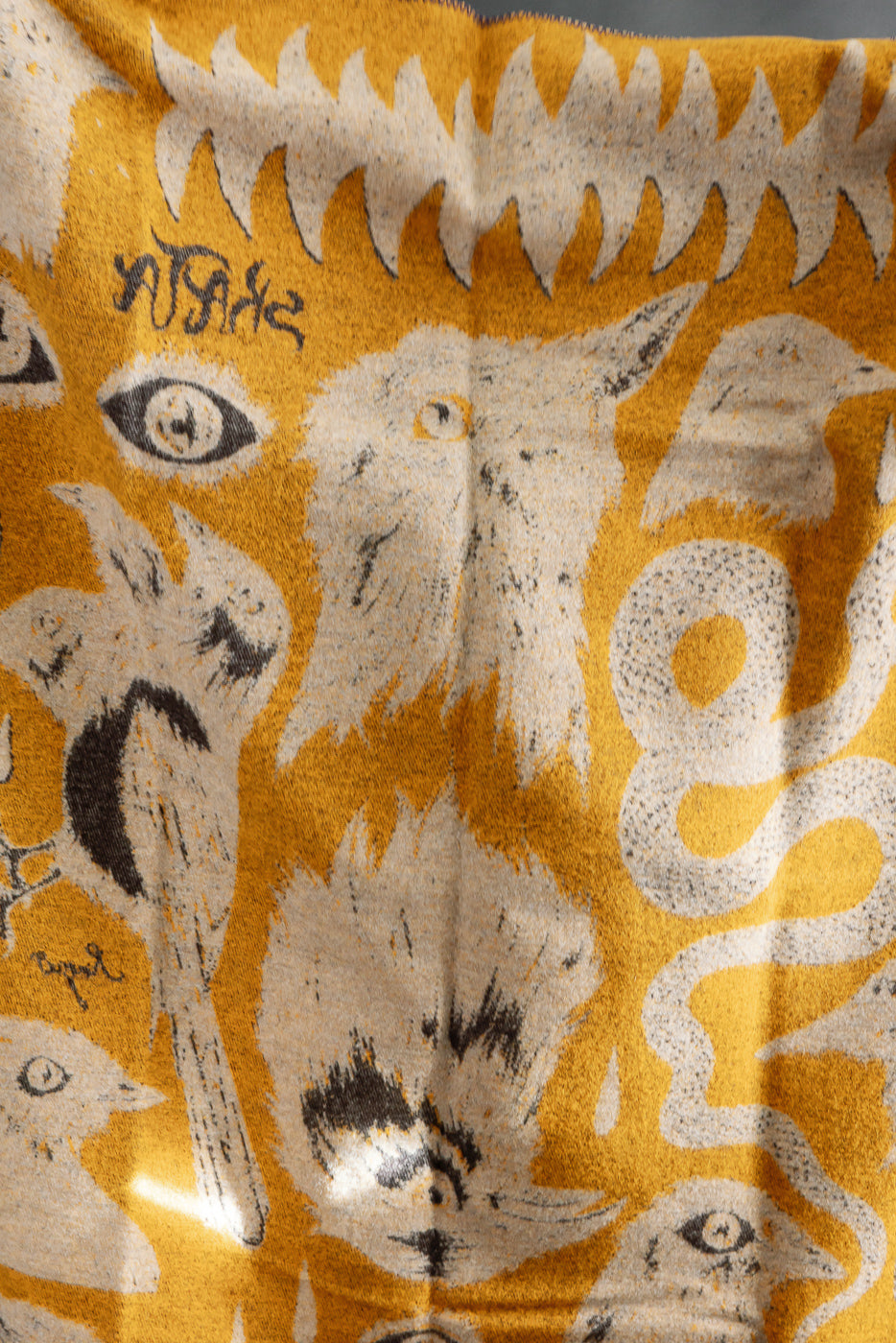 Close-up of Indigofera x Ragnar Persson Skata blanket, yellow-brown with illustrated animal motifs.