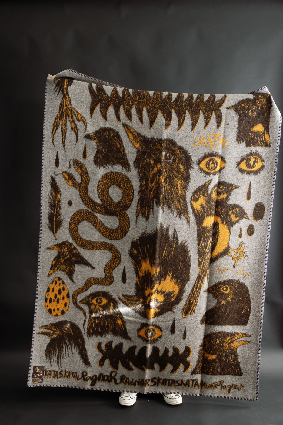 Indigofera Skata blanket grey brown yellow front view, graphic collab pattern, held by male model, full-body, contemporary accessory at Dant