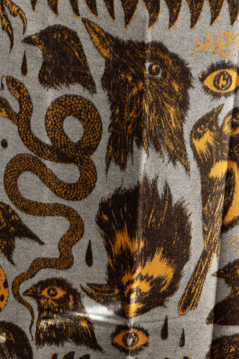Close-up of Indigofera Skata Blanket Ragnar Persson collab, grey with brown and yellow bird and snake motifs, detailed wool texture, front fabric view