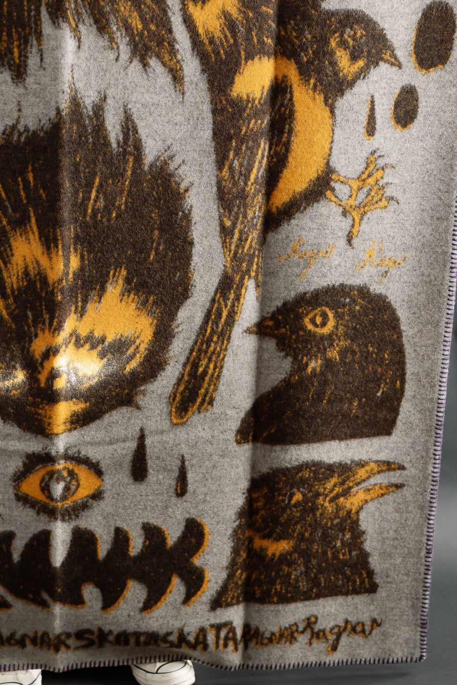 Close-up of Indigofera Skata blanket front, grey-brown-yellow pattern, soft wool texture.