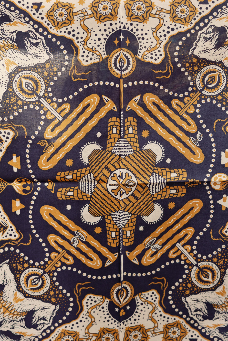 Front flat lay of patterned bandana with intricate orange and white designs on navy background