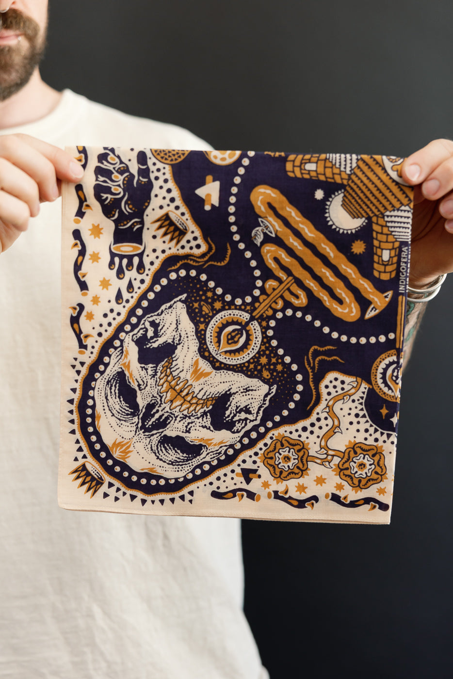 Male model holding patterned bandana, front view, skull and geometric design, navy and gold