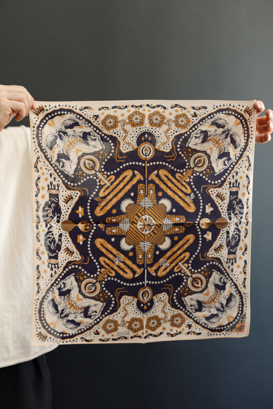 Front view of patterned bandana with skulls, geometric designs, and orange accents, held by male model.