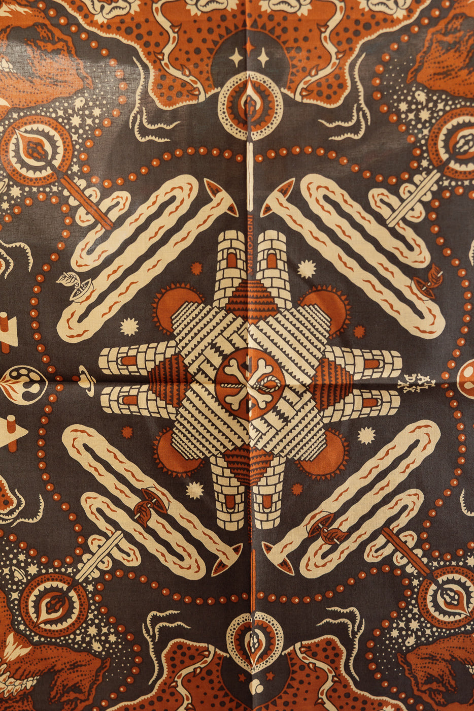 Front flat lay of patterned scarf with intricate orange, cream, and black designs, featuring geometric and symbolic motifs.