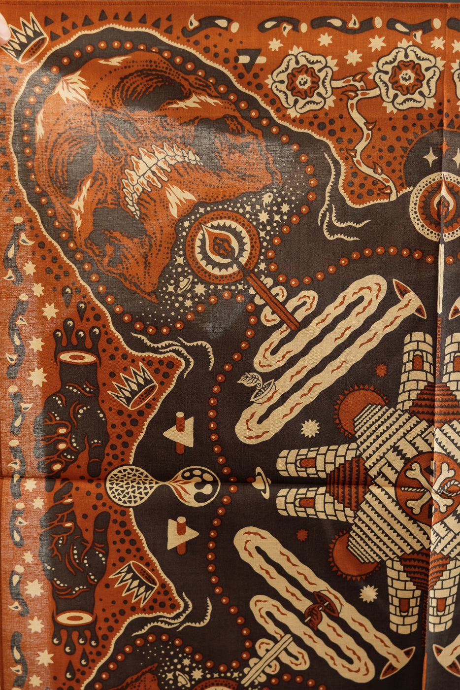 Close-up of front patterned scarf with skull, geometric designs, and intricate details in orange, black, and cream.