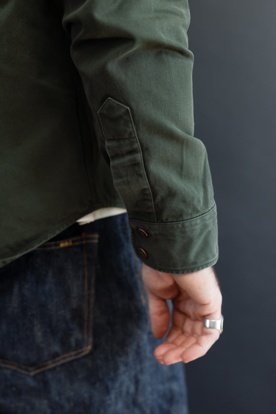 Close-up of the side view of a male model's sleeve on an olive green button-down shirt.