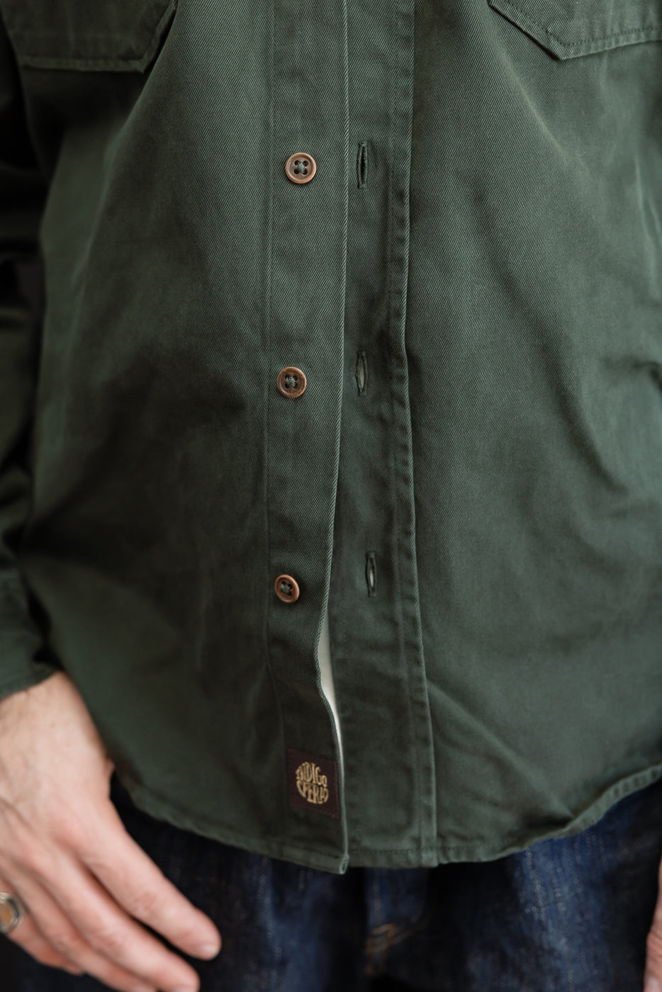 Close-up of the front of a dark green cotton shirt showing brown buttons and fabric texture.
