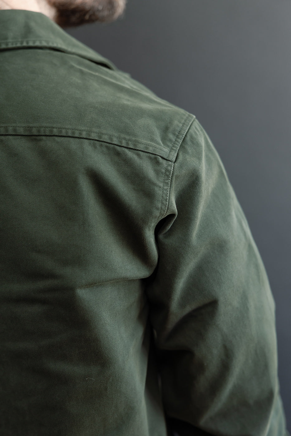 Close-up of the back and right shoulder of a green cotton canvas shirt showing fabric texture.