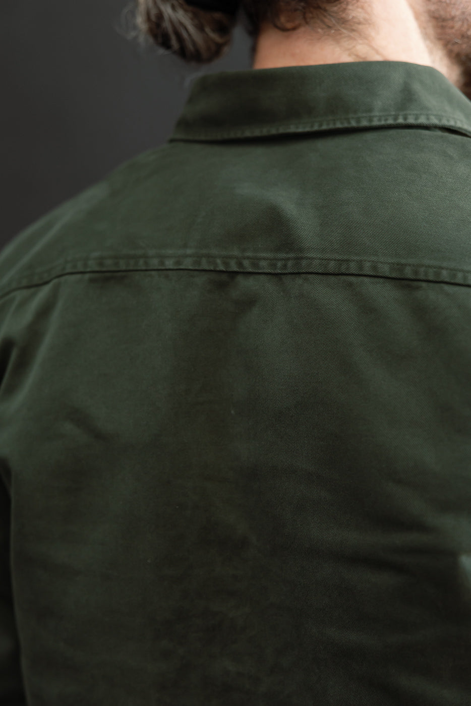 Close-up back view of a male model wearing a dark olive green cotton shirt showing the collar and shoulder seam.