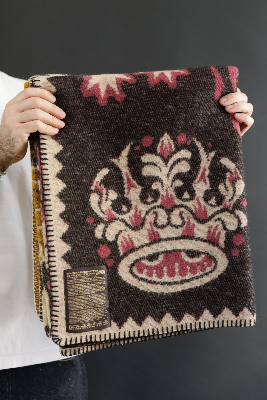 Front view of a folded brown wool blanket with a large pink crown pattern and serrated edges.