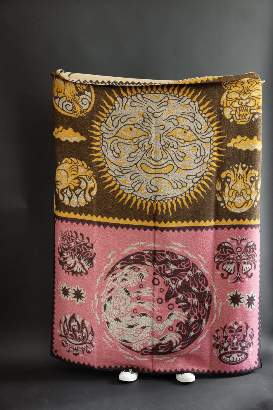 Front view of a woven tapestry blanket featuring a sun and moon celestial design in brown and pink.